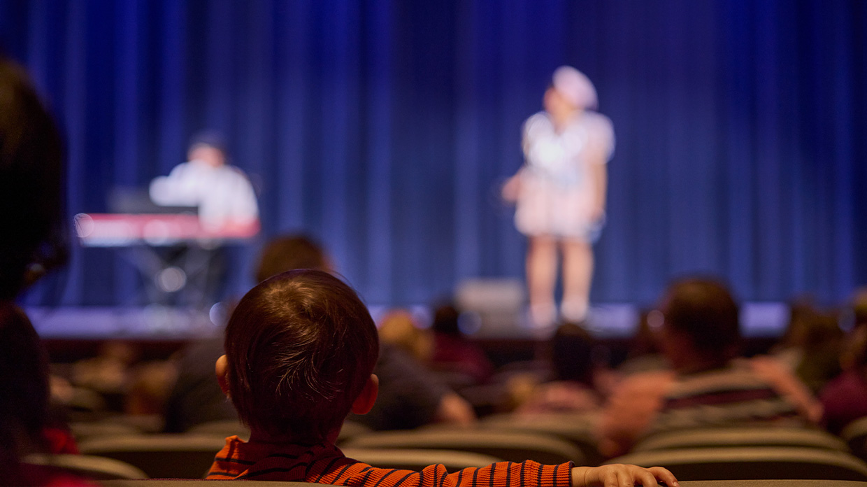 Child sat in an auditorium chair facing performers that are onstage