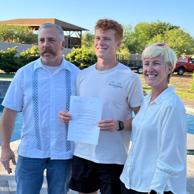 father, mother, and son posed for a photo with a letter in hand detailing the son was awarded a scholarship
